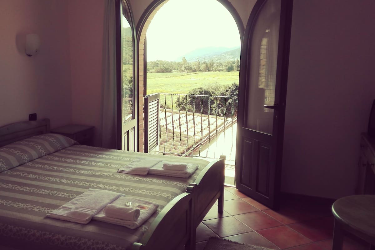 A bedroom with a bed, a nightstand, a chair, and a view of a balcony with a railing.