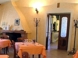 A dining area with tables covered in orange tablecloths, a fireplace, and a door leading to another room. - Hotel Janas (Tertenia)