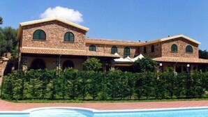 A large, multi-story stone building with a pool in the foreground. - Hotel Janas (Tertenia)