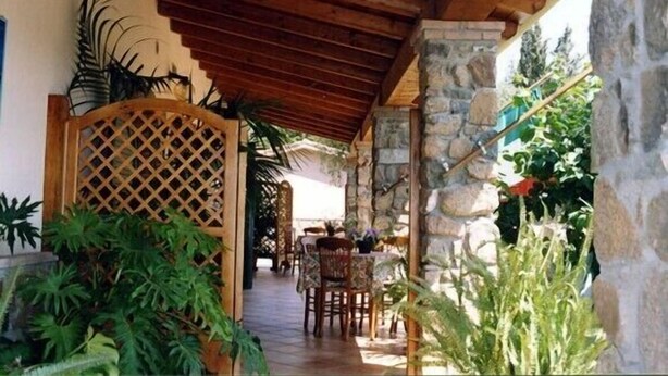 A covered outdoor area with wooden beams, stone pillars, and potted plants. - Hotel Janas (Tertenia)