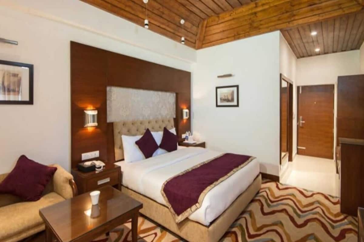 A hotel room with a bed, bedside tables, a nightstand, a chair, a desk, and a patterned rug.