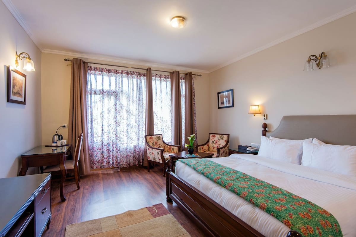 A hotel room with a bed, a desk, a chair, a lamp, and curtains.