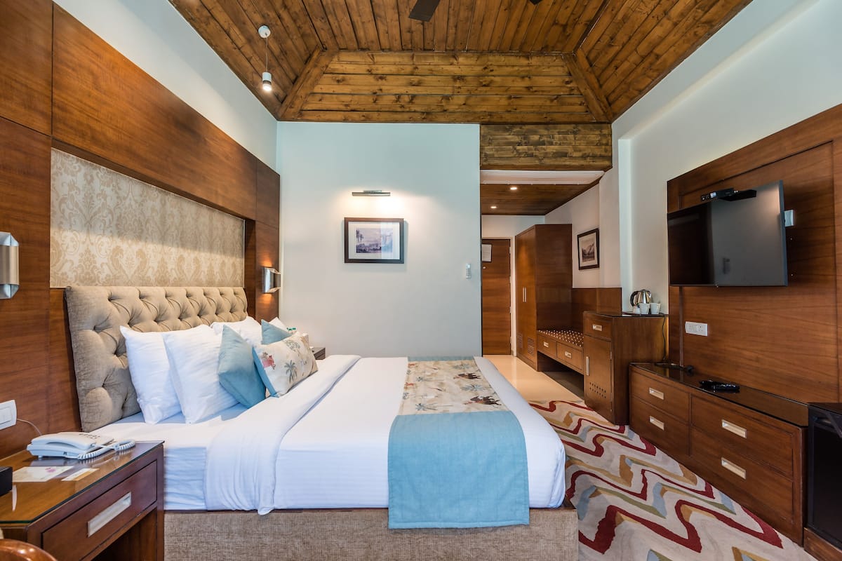 A hotel room with a large bed, wooden headboard, a television, and a wooden ceiling.