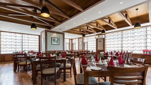 Un restaurant avec des tables et des chaises en bois, des luminaires suspendus et un mur décoré de motifs.