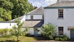 En toetages hvid bygning med en blå dør og vinduer, omgivet af grønt.