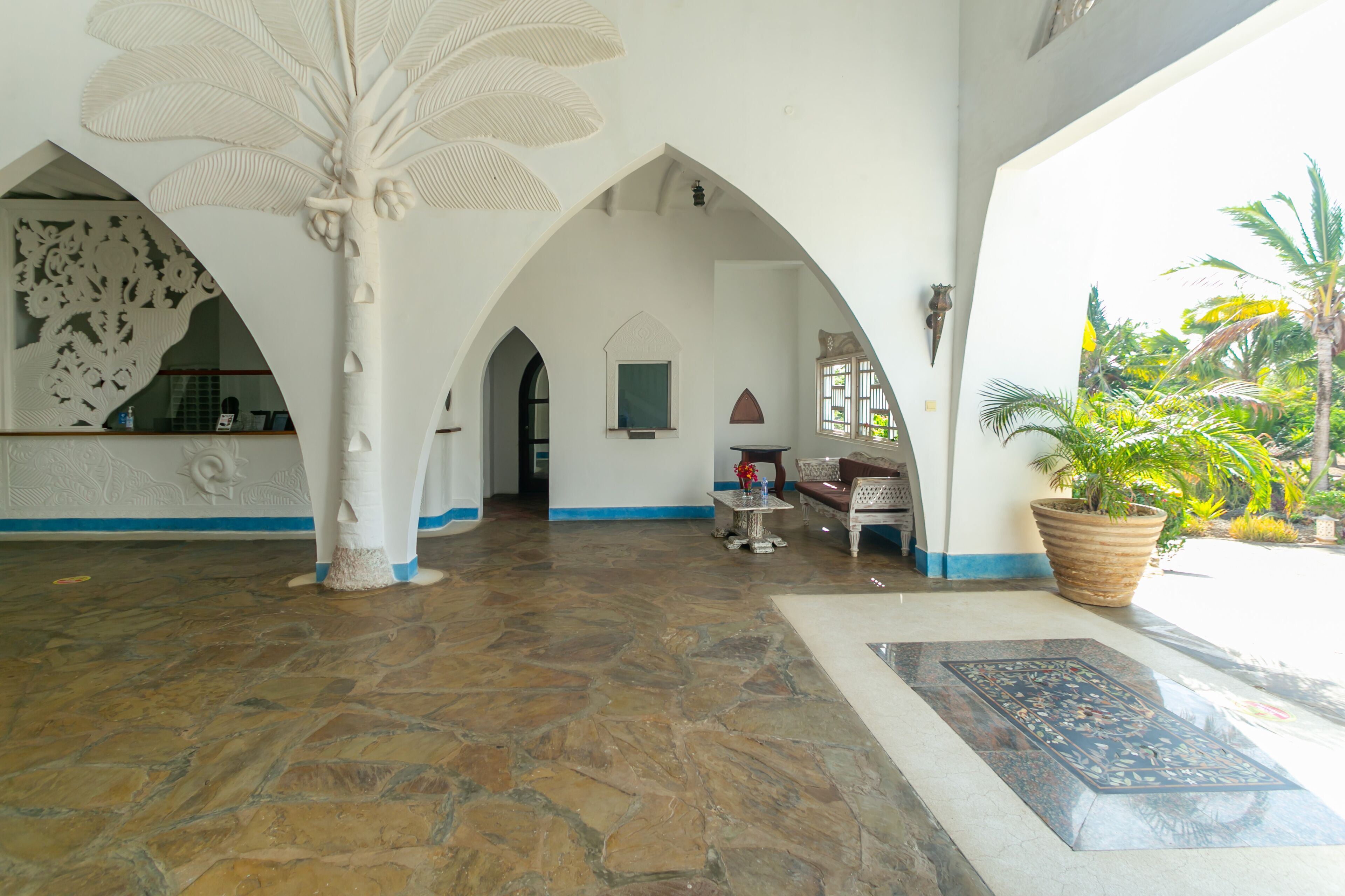 A spacious lobby with a stone floor, white walls, and a large tree sculpture. There are seating areas and a large potted plant.