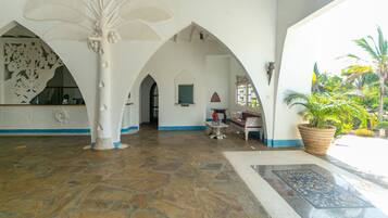 A spacious lobby with a stone floor, white walls, and a large tree sculpture. There are seating areas and a large potted plant.