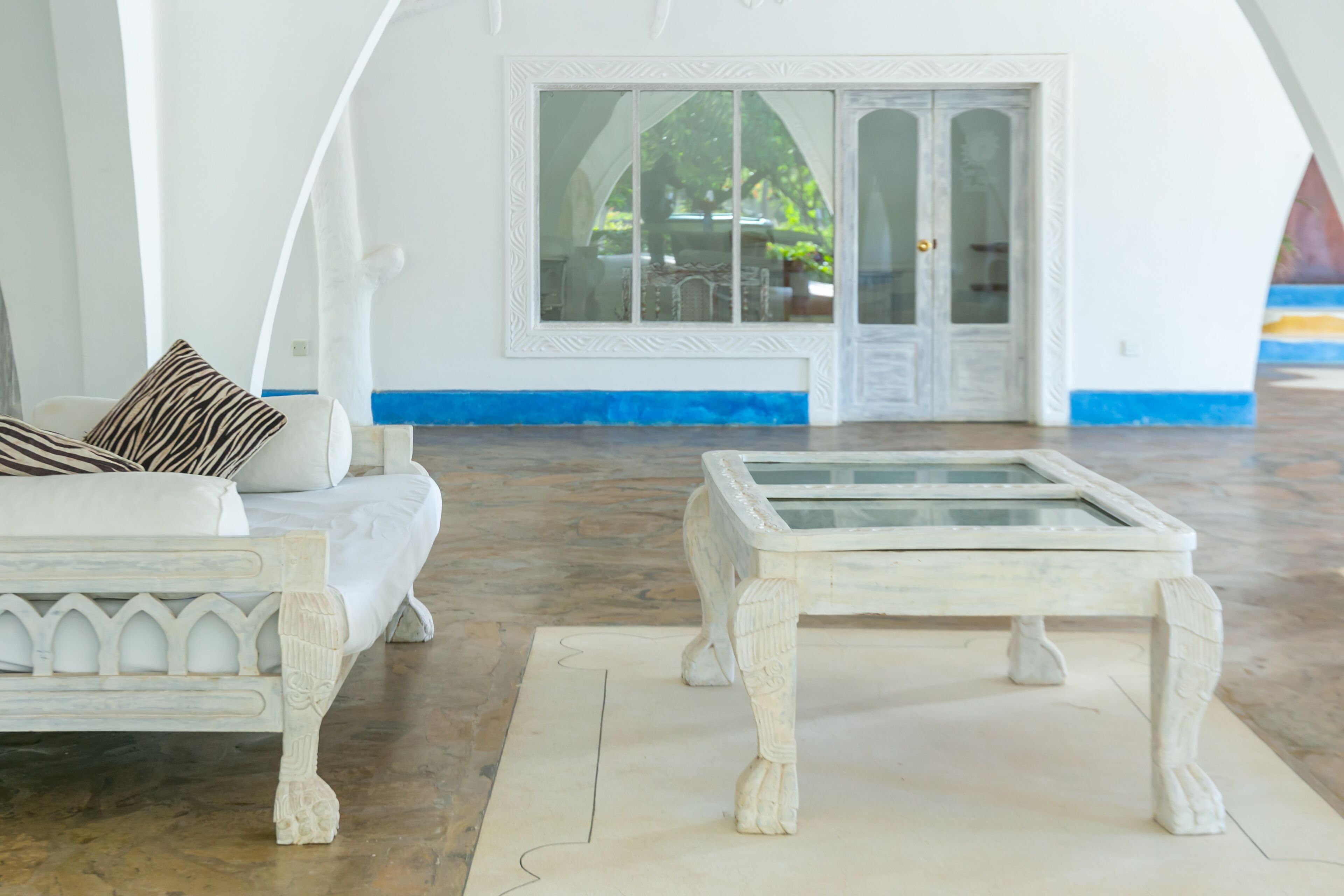 A white room with a bed, a glass-top table, and a door leading outside.