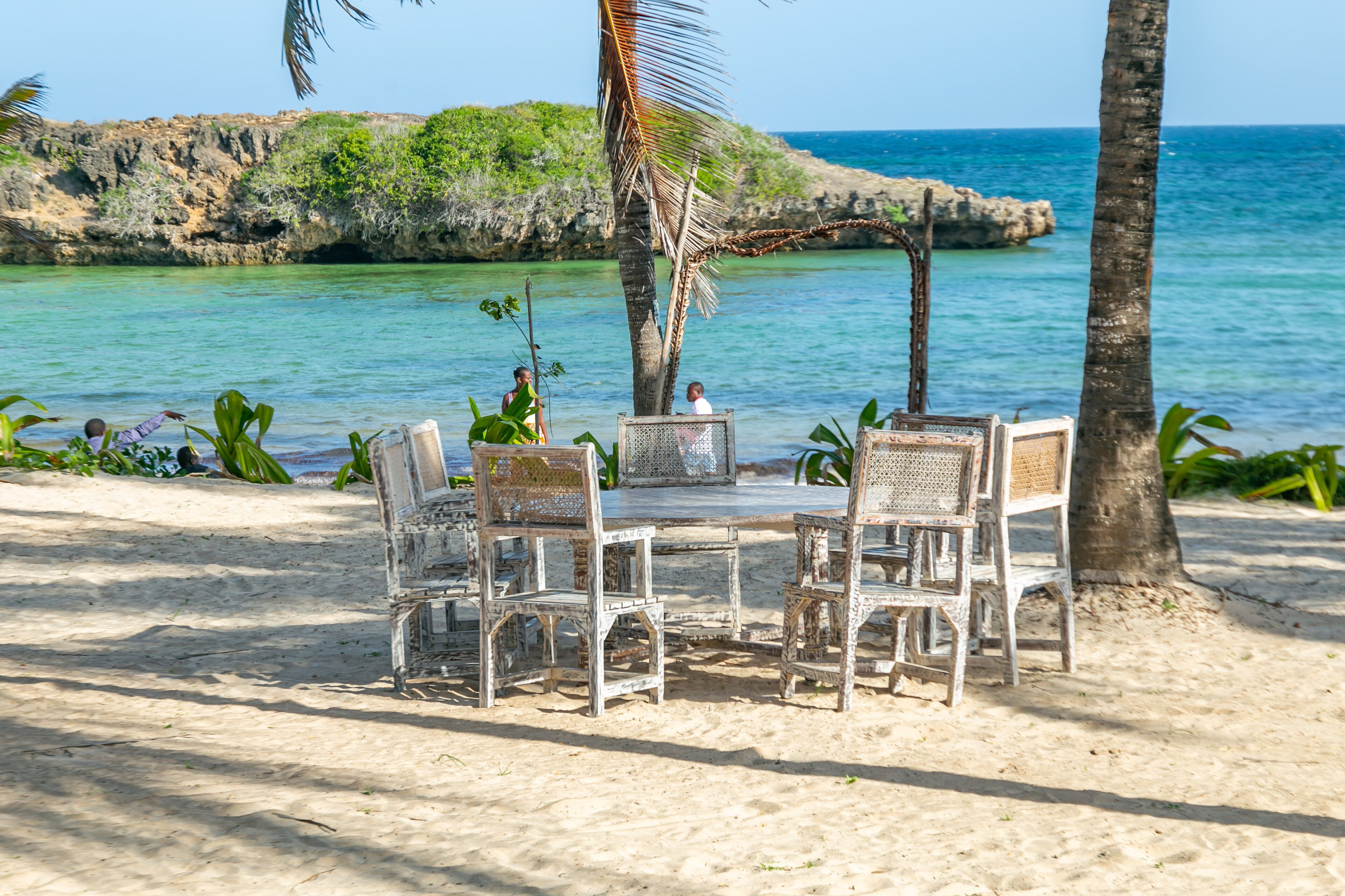 Une plage avec une table et des chaises, des palmiers et une vue sur l’océan.