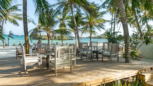 Une terrasse en bois, dotée de mobilier d’extérieur, de palmiers et offrant une vue sur l’océan.
