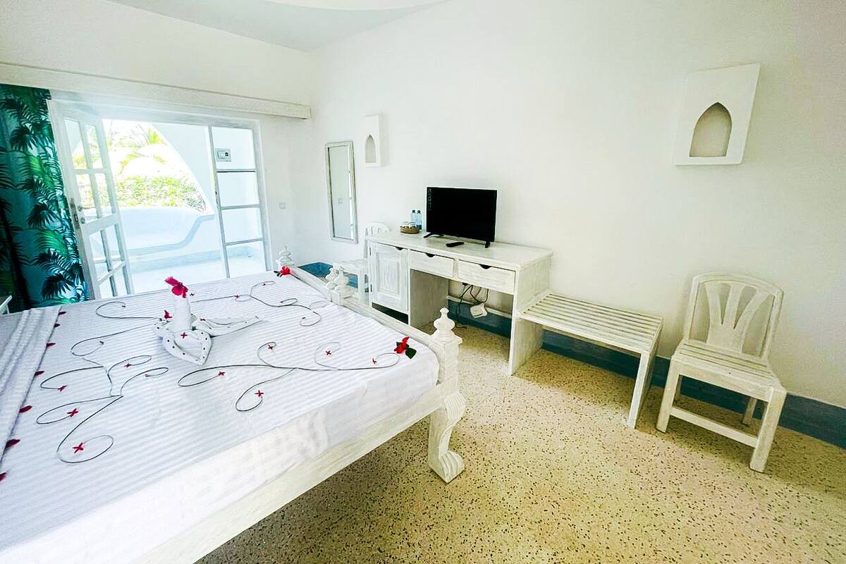 Um quarto com uma cama, uma escrivaninha, uma televisão e duas cadeiras.