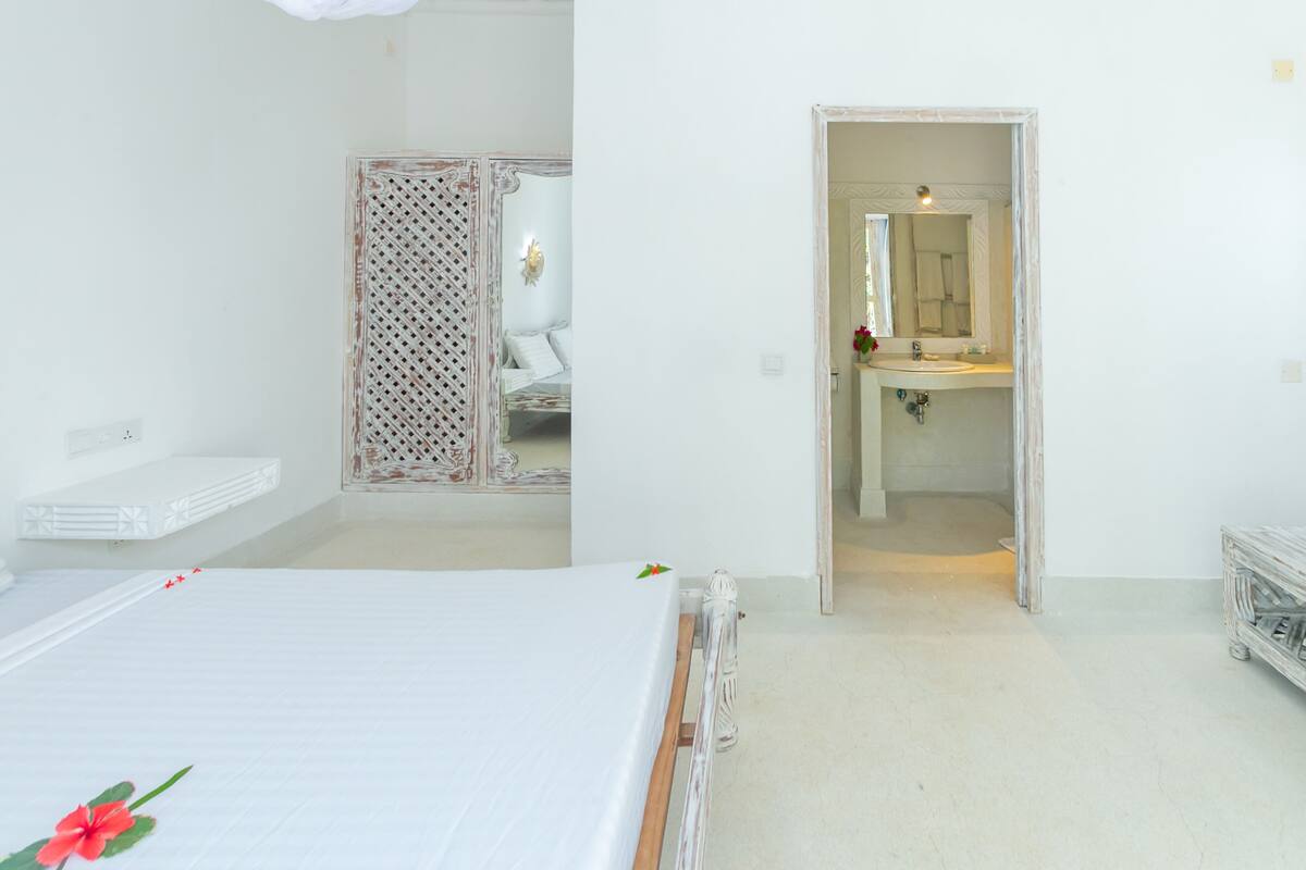 Quarto com cama, guarda-roupa e banheiro visível através de uma porta aberta.