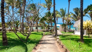 Un sentier de pierres mène à une zone située au bord de la plage, agrémentée de palmiers et offrant une vue sur l’océan.