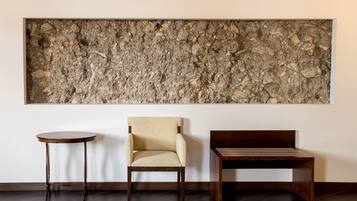 Una habitación con un cuadro de pared grande y con textura, una mesa redonda de madera, un sillón color beige y un banco de madera.