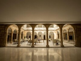 Un amplio patio con múltiples arcos y columnas, que incluye una zona de estar central con mesas y sillas.