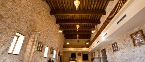 A spacious hall with stone walls, wooden beams, and chandeliers.