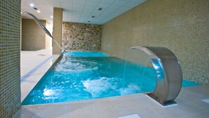 Una piscina interior con pared de piedra y suelo de baldosas.