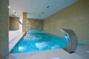 Una piscina interior con pared de piedra y suelo de baldosas.
