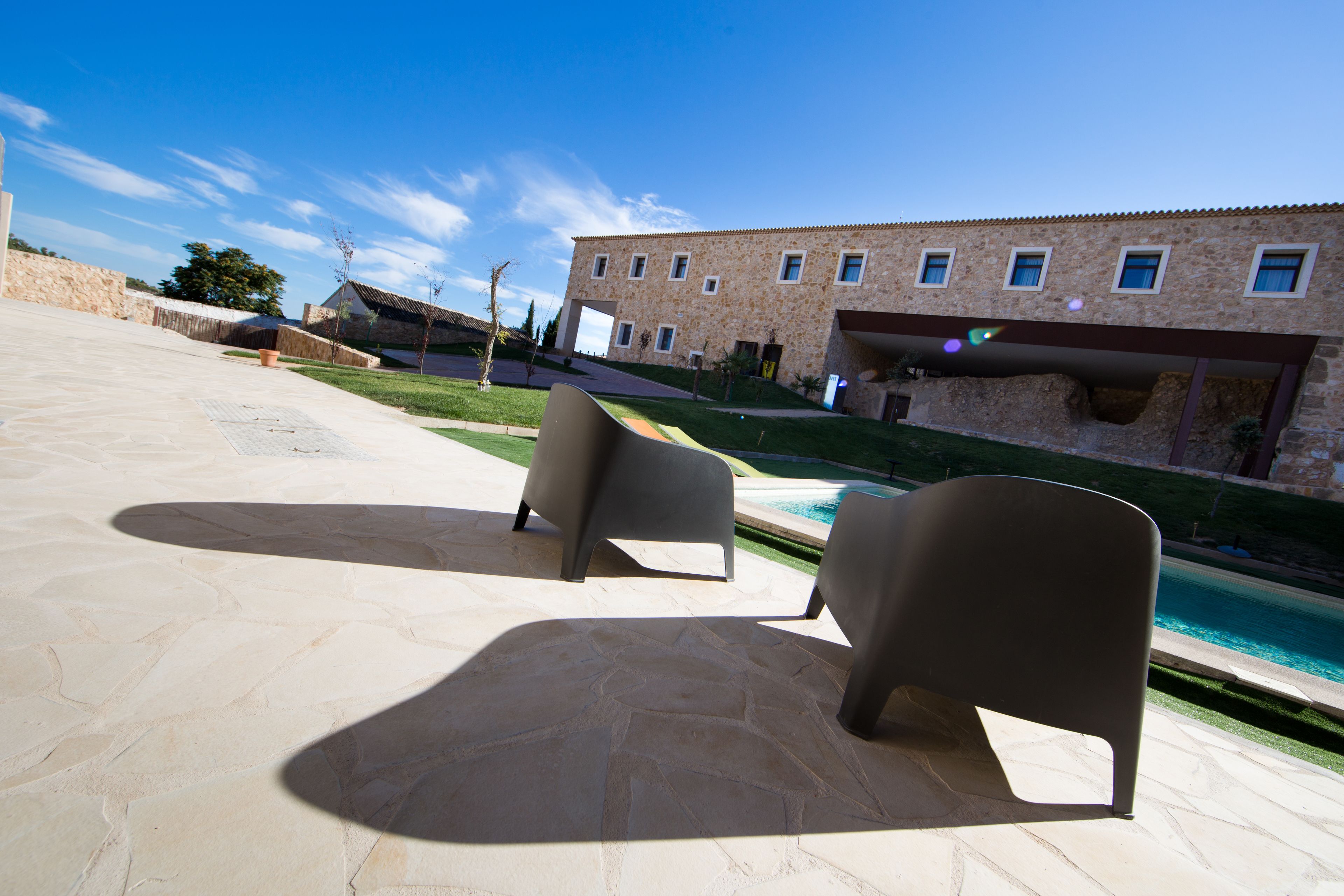 A poolside area with two lounge chairs, a stone patio, and a building with multiple windows and a covered entrance.