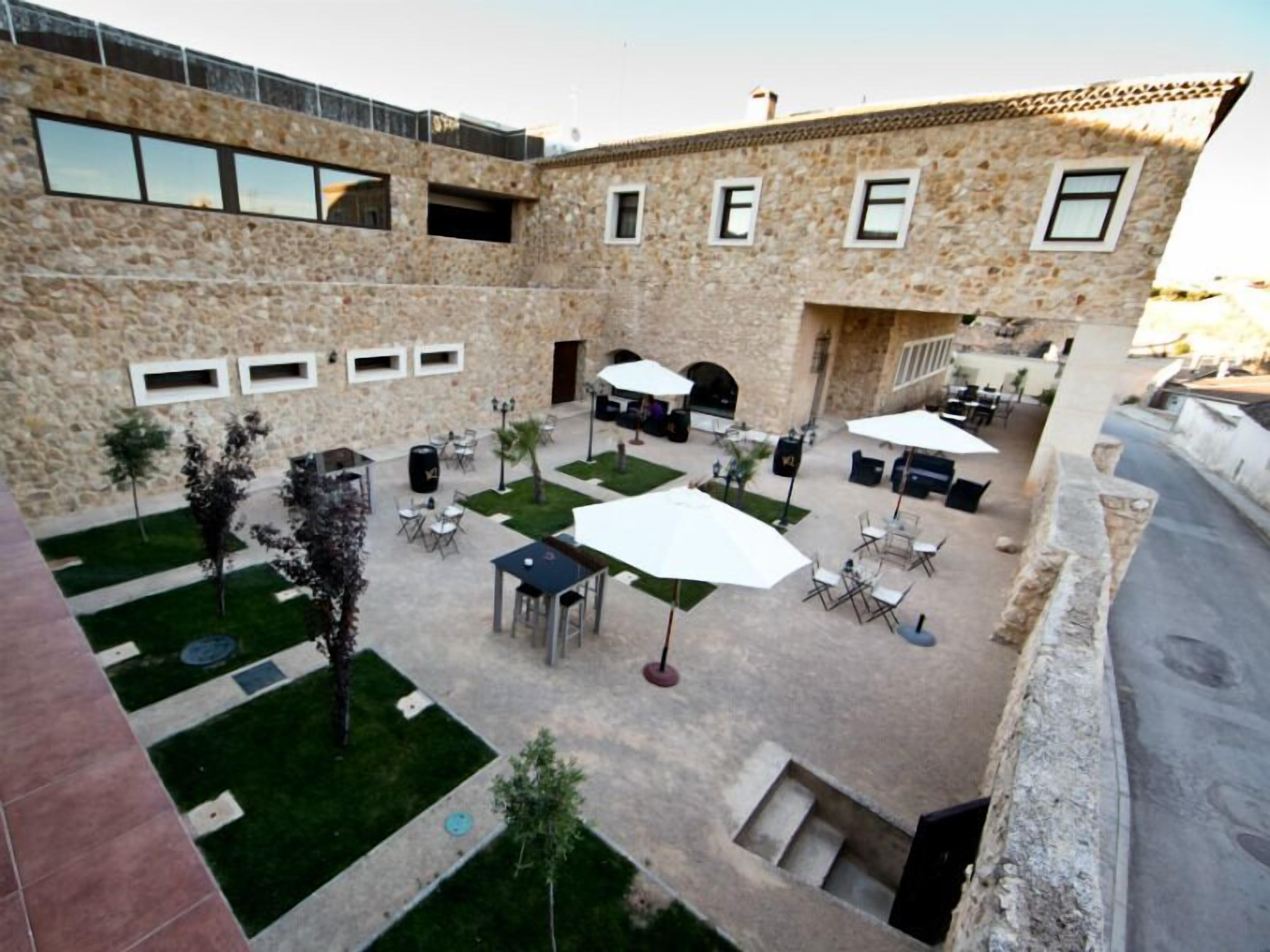 Un patio con mobiliario exterior, paredes de piedra y un edificio de piedra con ventanas.