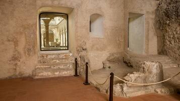 A historical building interior with stone walls, a tiled floor, and a rope barrier.