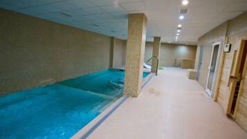 An indoor swimming pool with tiled walls and a tiled floor, a central column, and a door on the right.