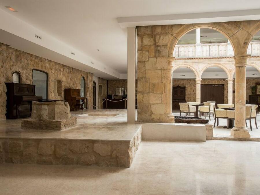 A spacious lobby with stone walls, a marble floor, and a central seating area with tables and chairs.