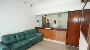 A reception area with a wooden desk, two individuals behind it, and a green sofa. - Hotel Lotte (Ipoh)