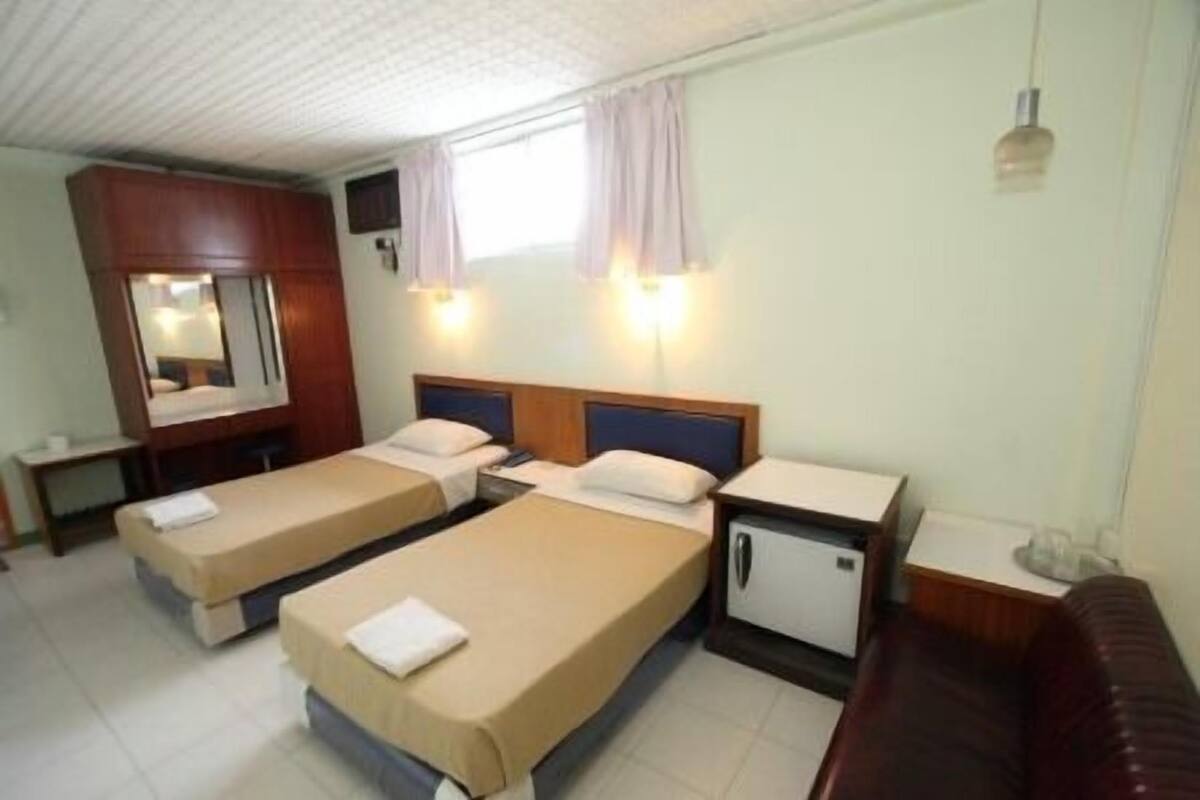 A hotel room with two single beds, a small desk, a mirror, and a nightstand with a lamp.