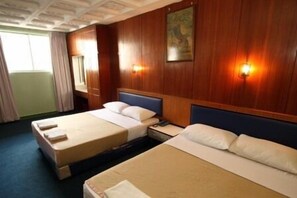Une chambre d’hôtel avec deux lits, des boiseries, un tableau au mur et une table de chevet avec un téléphone.