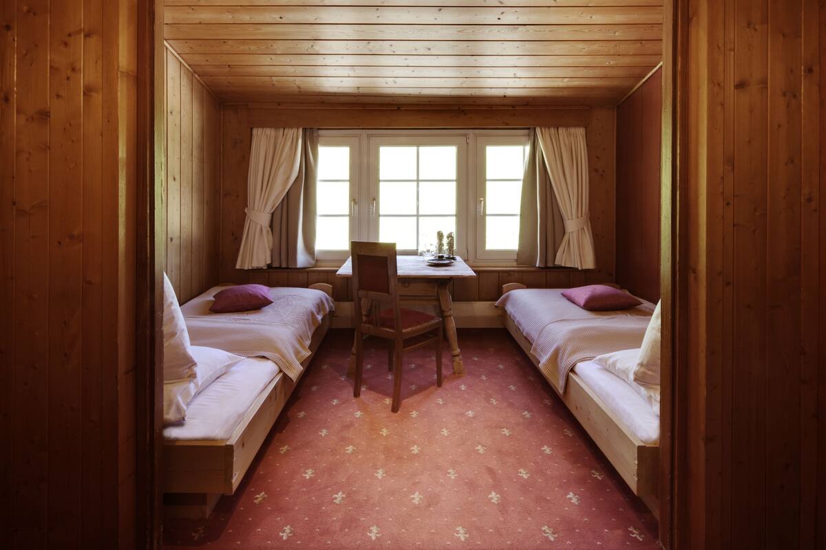 A small room with two wooden beds, a wooden desk, and a chair.