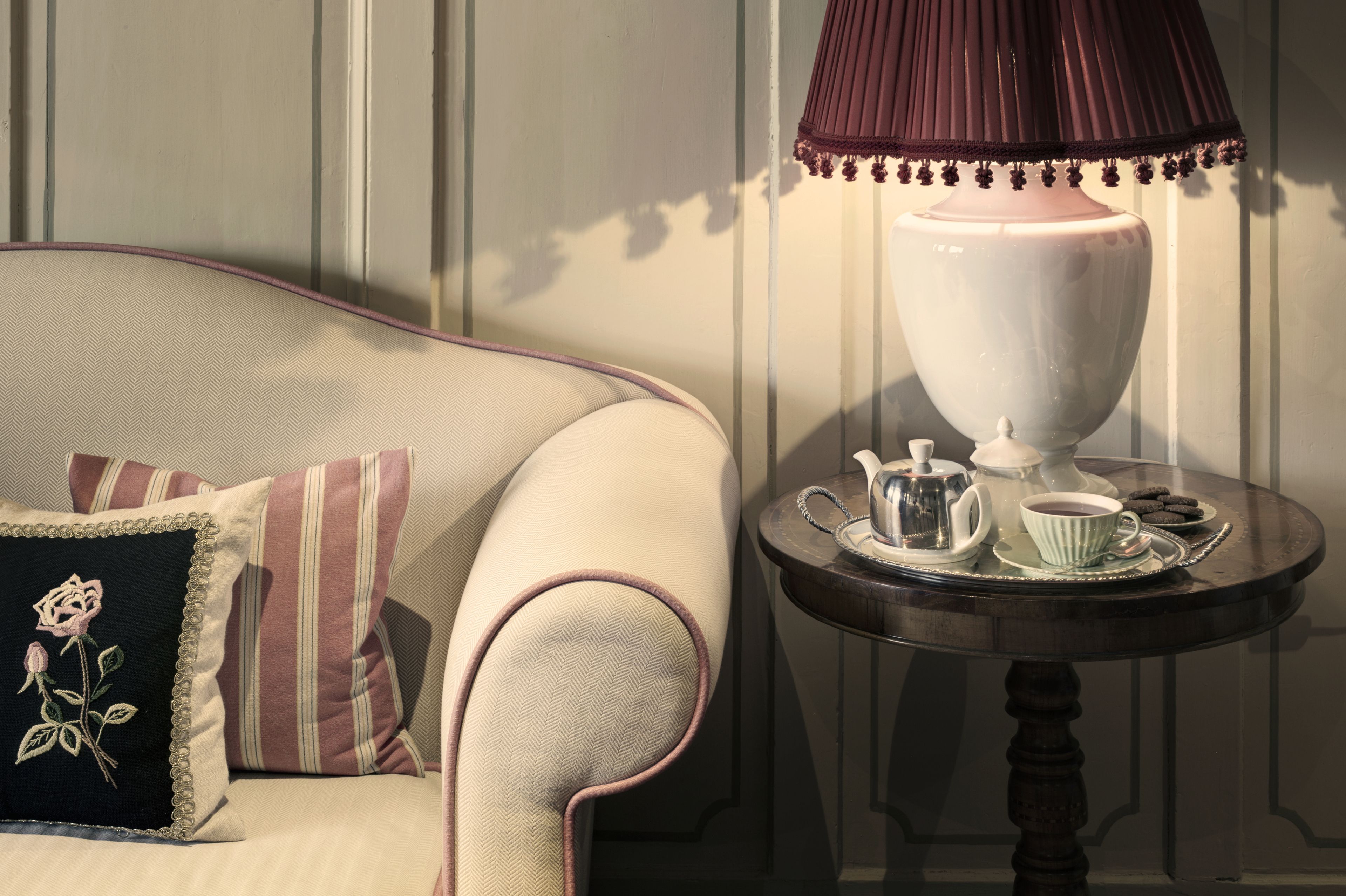 Une pièce chaleureuse avec un canapé, une table sur laquelle se trouvent une théière, des tasses et des biscuits, ainsi qu’une lampe décorative.