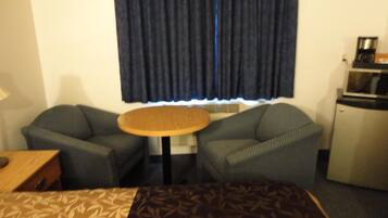 Habitación de hotel con cama, dos sillones, una mesita redonda, microondas y ventana con cortinas.