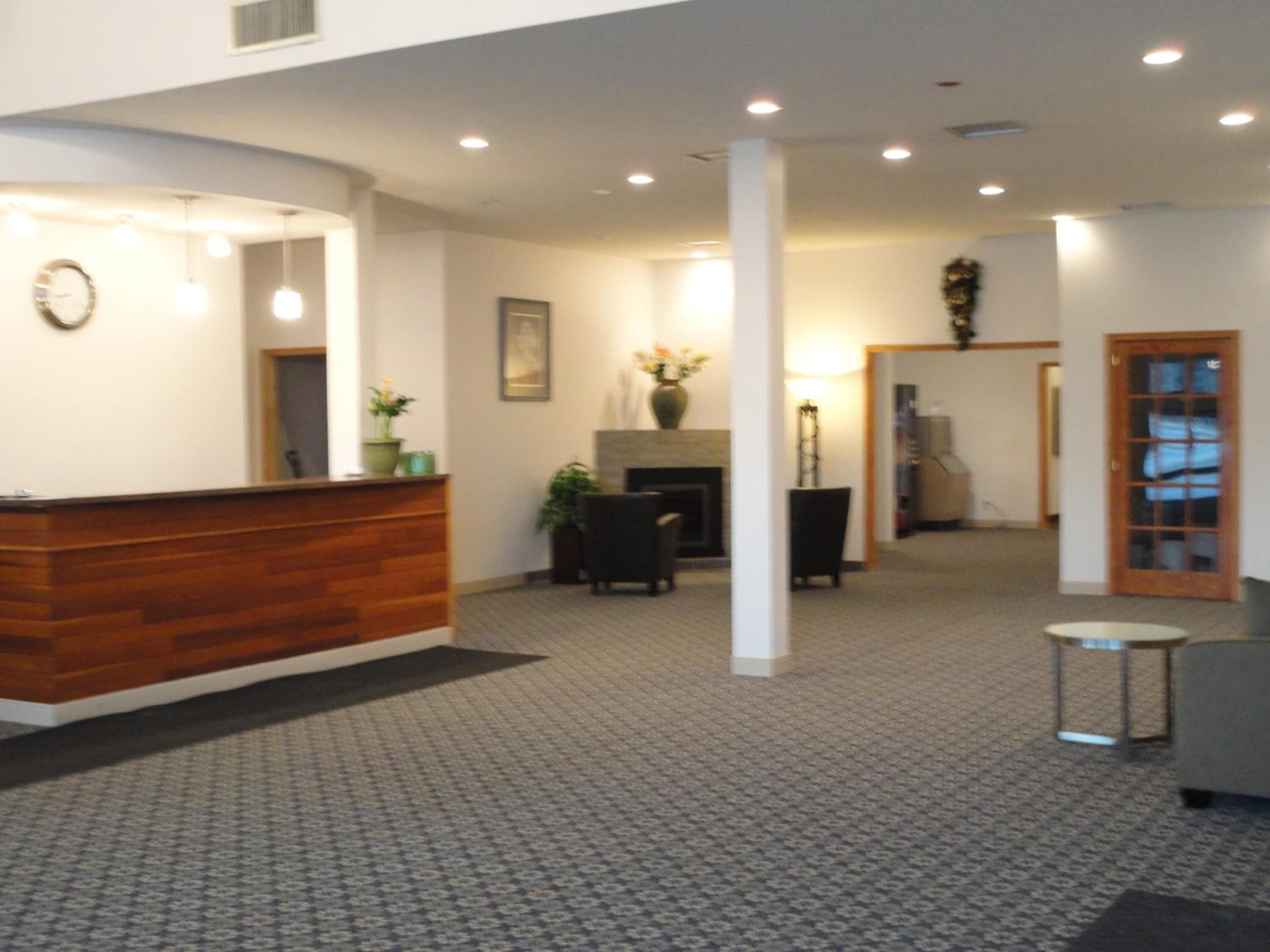 A reception area with a wooden reception desk, a clock, and a vase with flowers. There is a fireplace and a chair in the background.