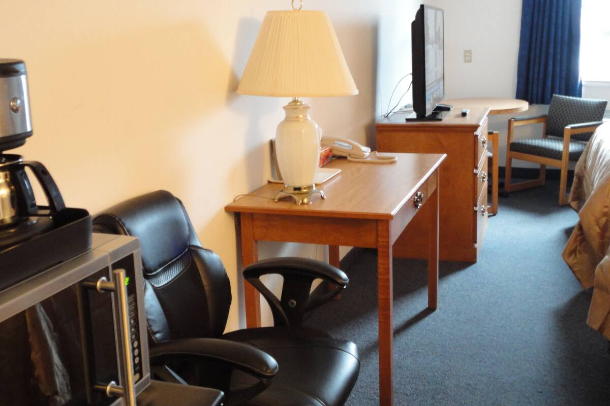 Ein Hotelzimmer mit Schreibtisch, zwei Stühlen, einer Lampe, einem Fernseher und einer Kaffeemaschine.