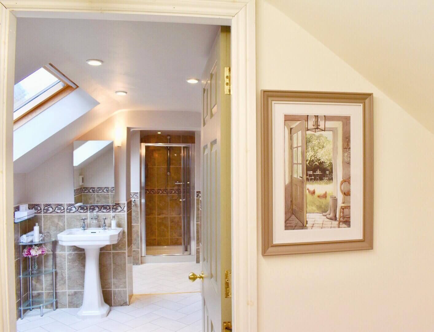 A bathroom with a skylight, a pedestal sink, and a shower enclosure.