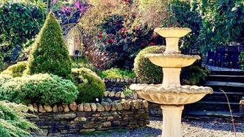 Um jardim com uma fonte de pedra, um muro de pedra e diversas plantas.