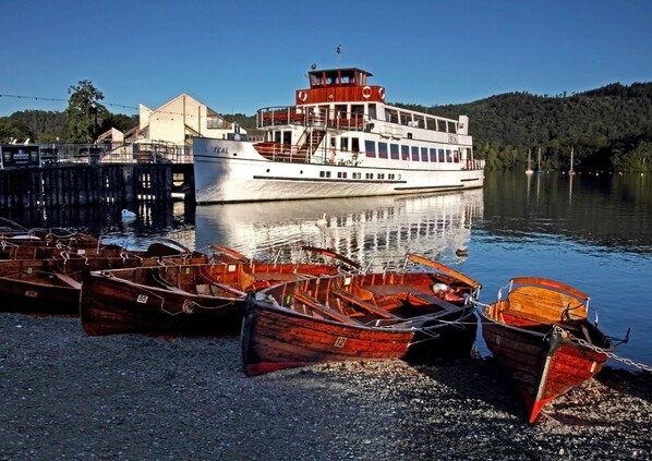 Un bote blanco grande amarrado en un muelle, con una estructura tipo cabaña en la parte superior. Varias embarcaciones de madera más pequeñas están alineadas en la orilla.