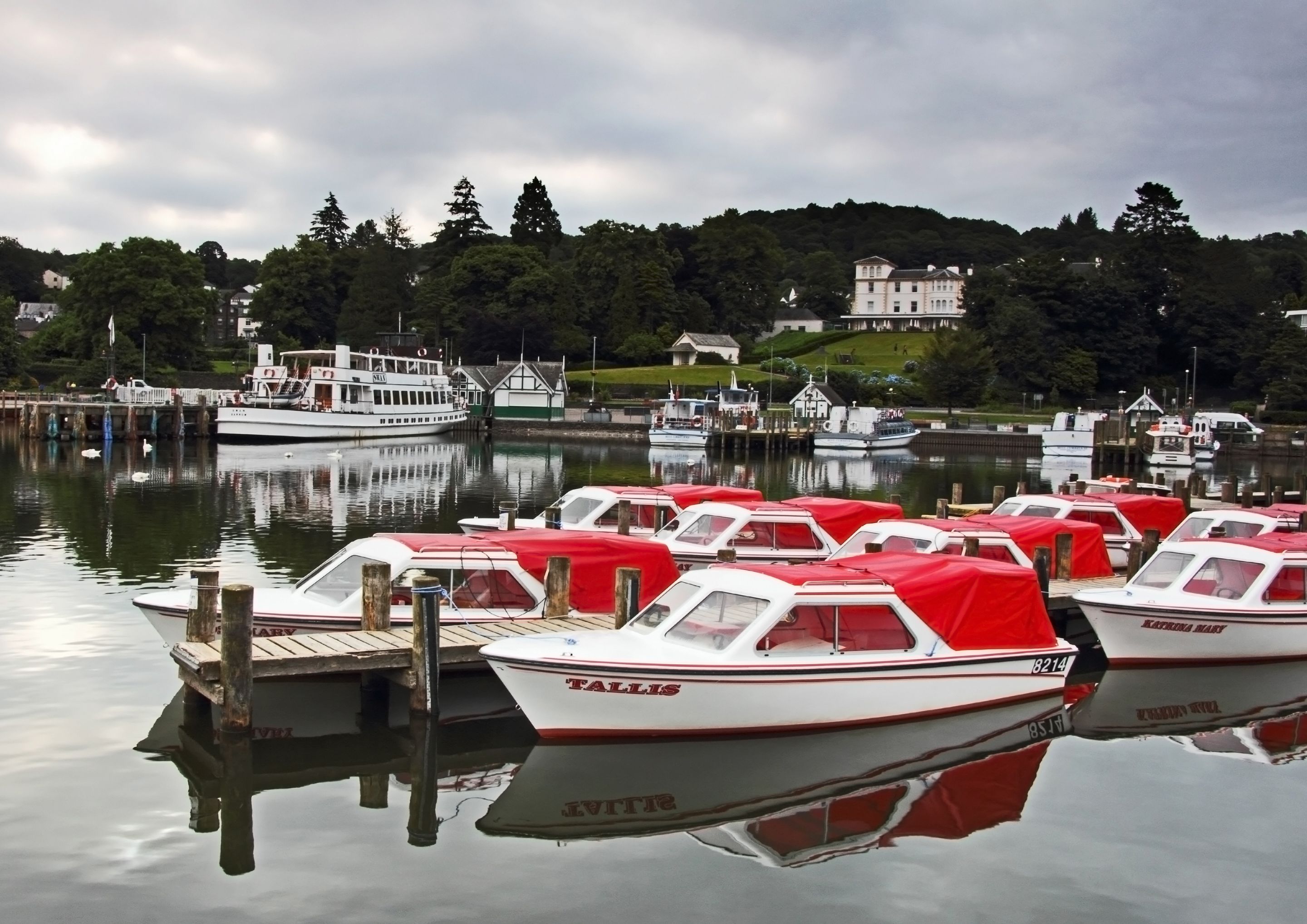 A marina with several small boats docked, a large white boat in the background, and a building with a green roof on the shore.