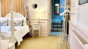 A bedroom with a four-poster bed, a bedside table, a lamp, and a hanging mirror.