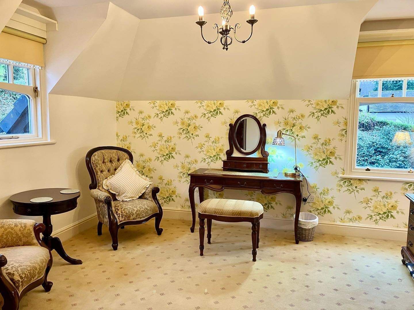 Quarto com lustre, escrivaninha com espelho, duas cadeiras e janela com vista para o verde.