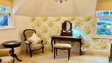 Quarto com lustre, escrivaninha com espelho, duas cadeiras e janela com vista para o verde.