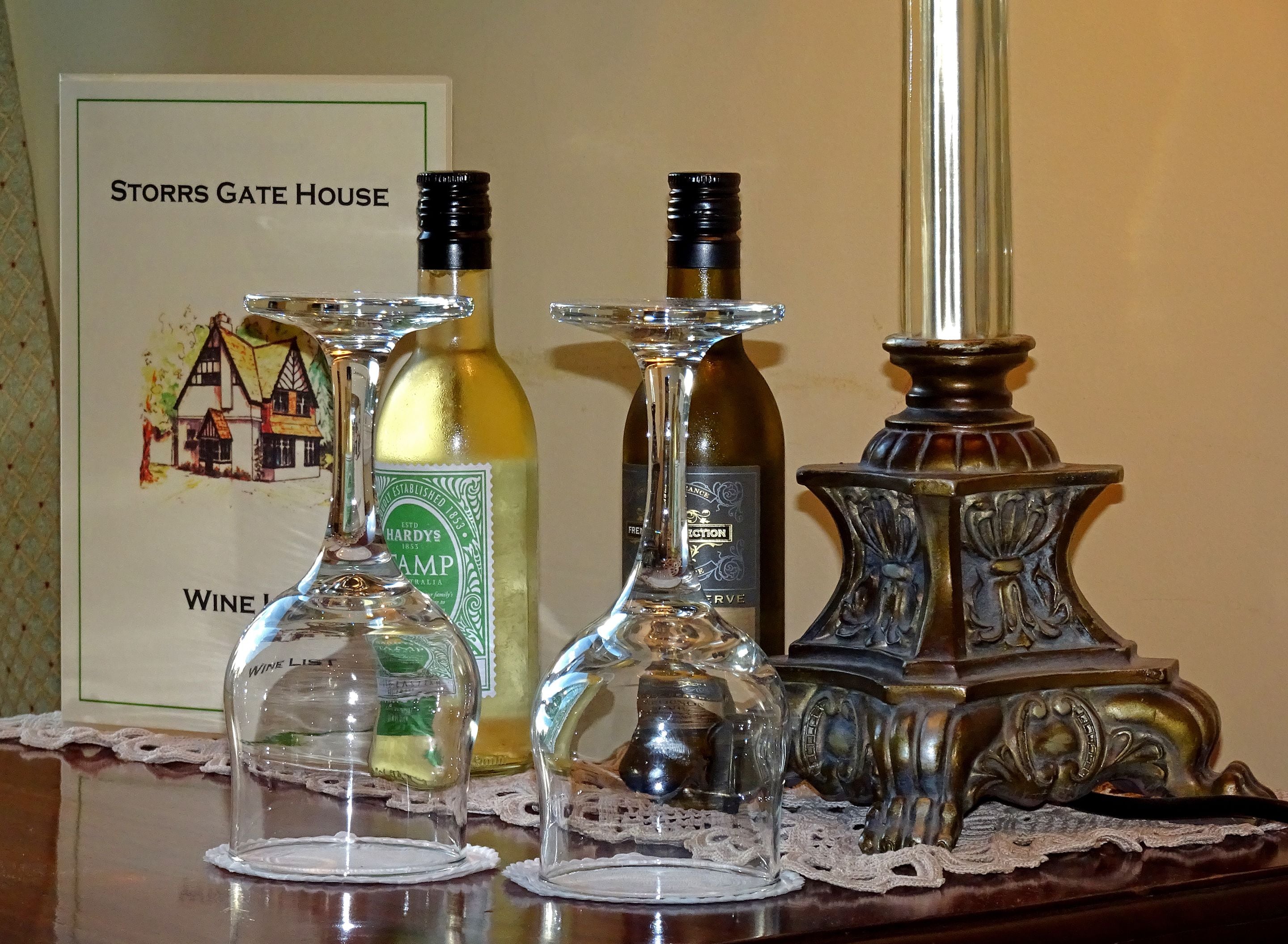 A table with three wine glasses and a candle holder. A sign with a house illustration and text is visible in the background.