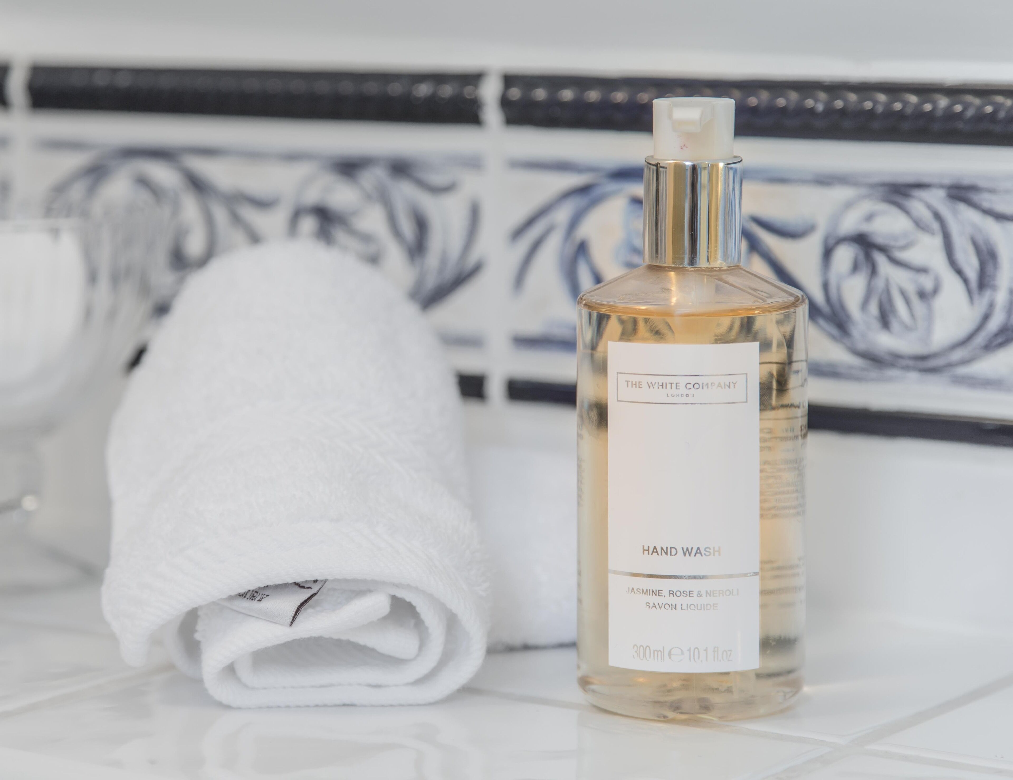 A bottle of hand wash soap next to a folded white towel on a tiled surface.