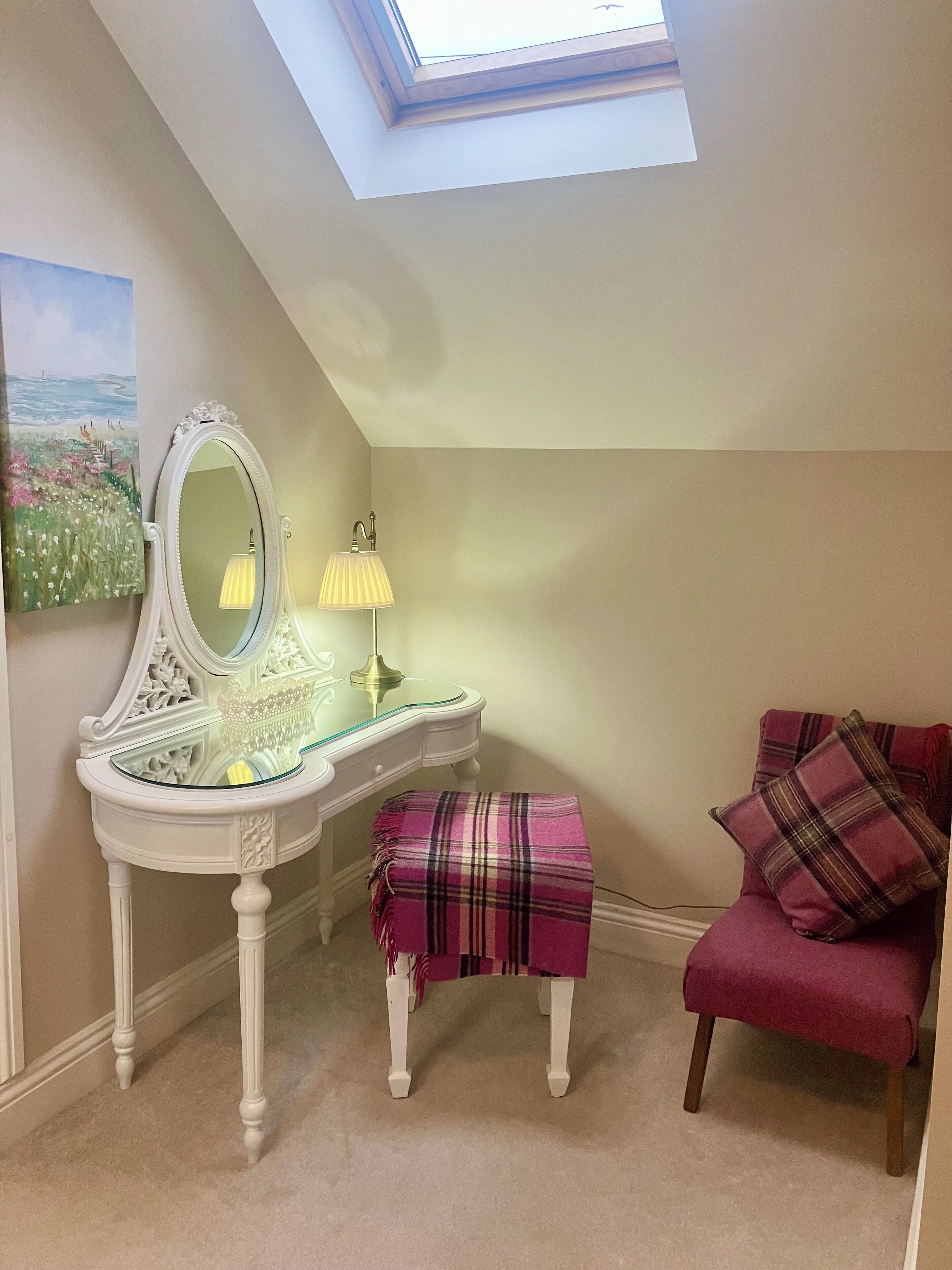 A room with a skylight, a vanity with a mirror, a lamp, a bench, and a chair.