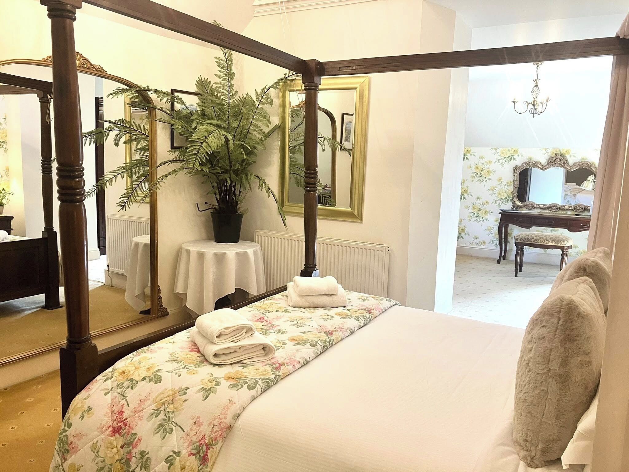 Una cama con dosel con una colcha estampada, una planta en maceta, un espejo y un aparador con espejo.