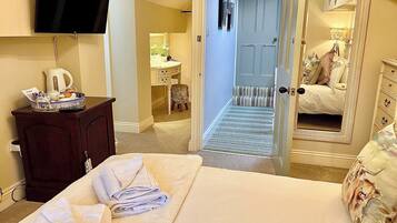 A hotel room with a bed, a TV mounted on the wall, a desk with a kettle, and a bathroom visible through an open door.