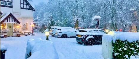 A snow-covered landscape with a traditional building, parked cars, and a water tower.