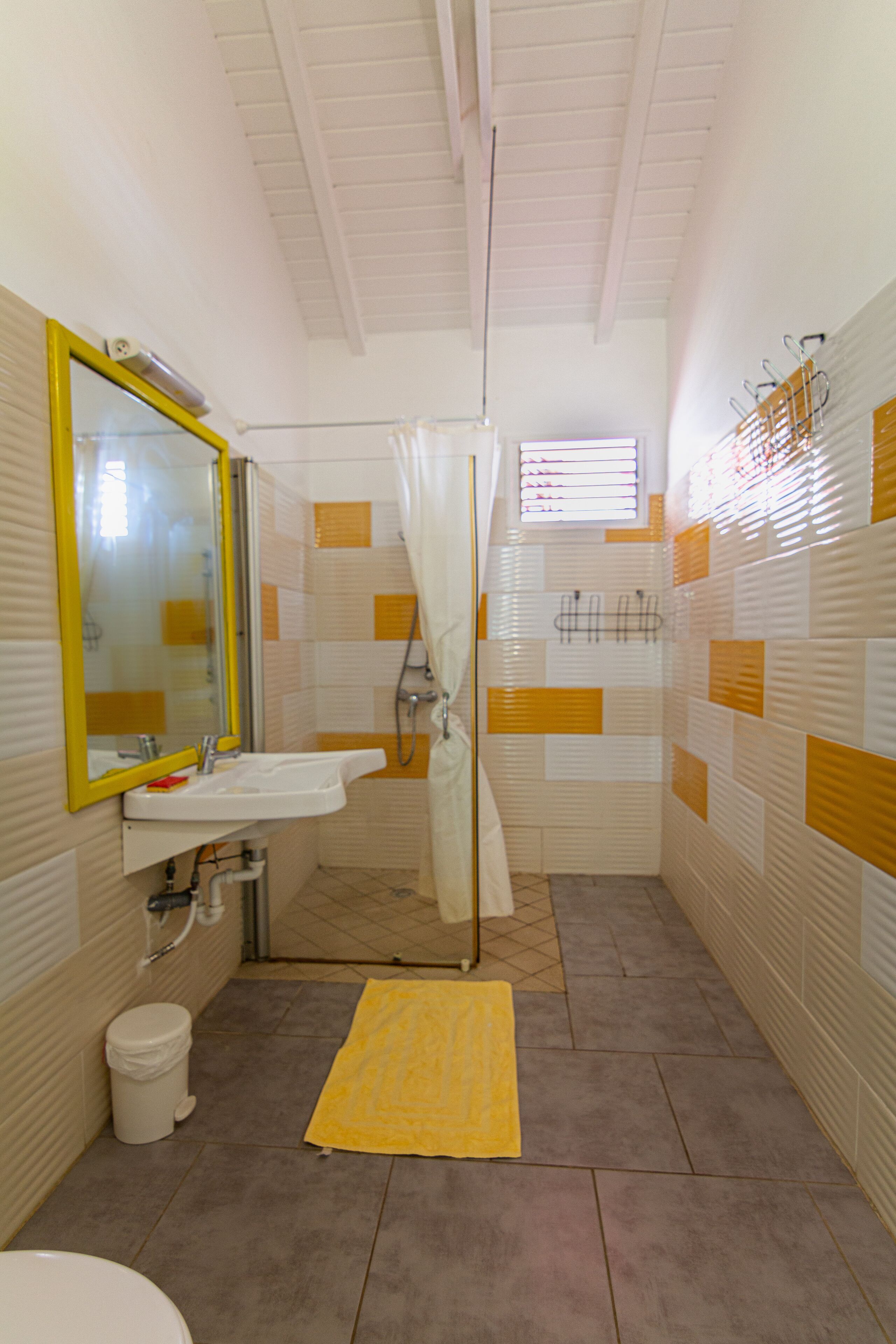 A bathroom with a yellow-tiled shower, a white sink with a yellow mirror, and a yellow bath mat.