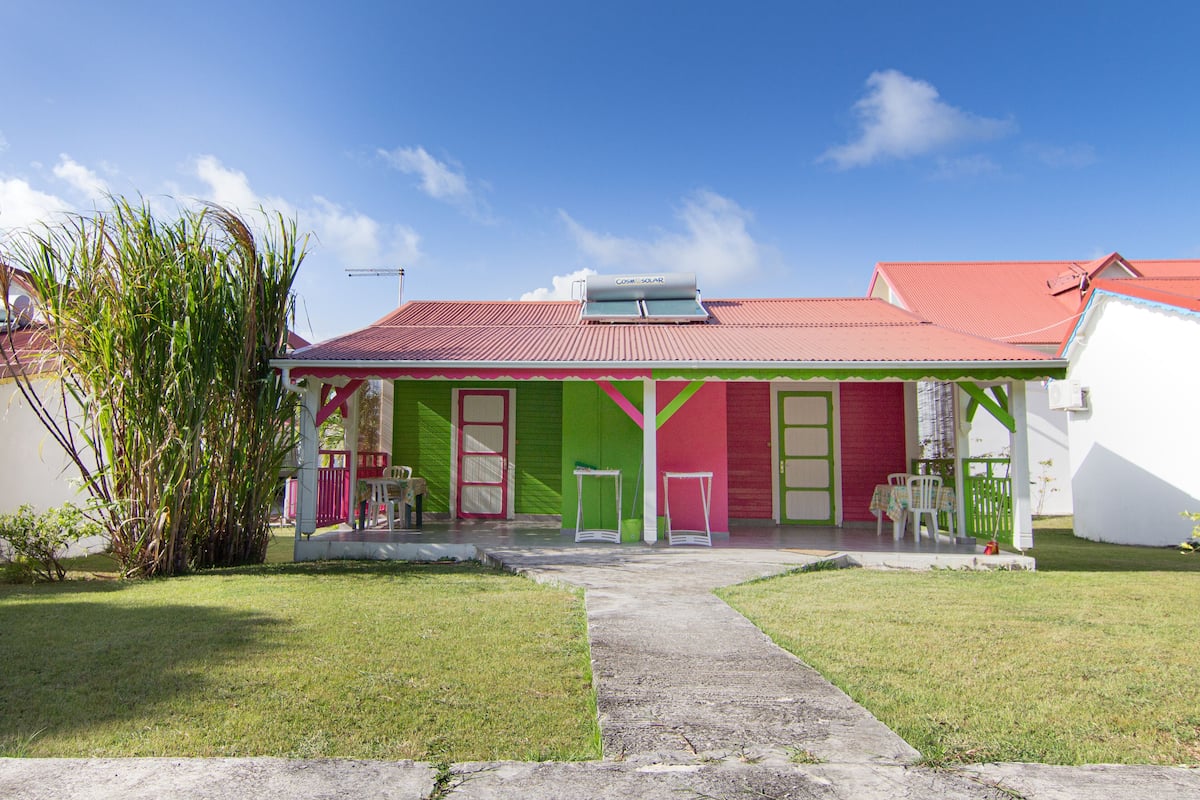 Ein buntes Haus mit rotem Dach, grünen und rosa Wänden und einer kleinen Veranda mit Stühlen und einem Tisch.